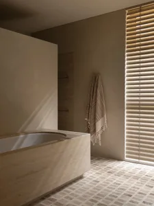 A well-lit bathroom with a beige color scheme, a bathtub, and a towel, featuring natural stone or tile materials and a window