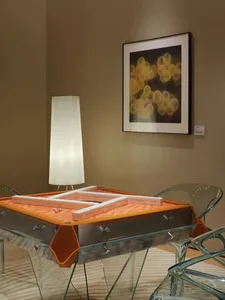 A well-lit living room with a glass dining table, two chairs, a couch, and a lamp, featuring glass and wood materials