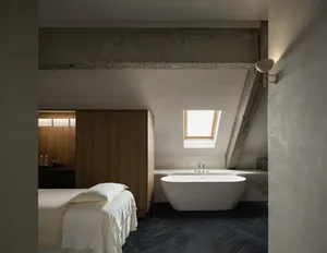 Bright and airy bedroom with a white color scheme, a bed near the window, and a bathtub in the corner