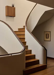A modern staircase with a wooden railing in a residential hallway, bathed in natural light
