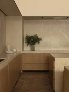 A modern kitchen with a white marble countertop, brown wooden cabinets, and natural light from a window