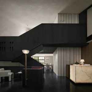 A dimly lit modern living room with a wooden staircase, black railing, and black and white color scheme, featuring two couches and a chair arranged around the staircase
