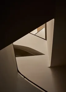 A dimly lit staircase with a curved design, set against a white wall and a darker wall, in a modern building with a minimalist aesthetic