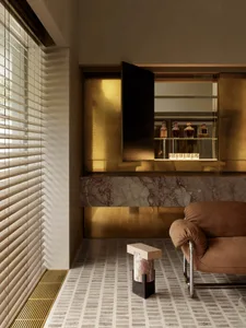 Warm and inviting living room with a marble floor, gold wall, and brown chair, featuring a dining table with bottles and a vase on the floor
