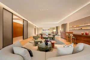 A modern living room with a large open floor plan, featuring comfortable seating areas, potted plants, and decorative vases, set against a neutral background