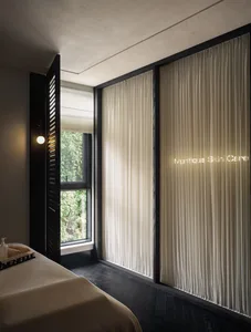 A calm and inviting spa or salon space with a white curtain, black door, and natural light from a large window