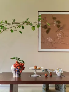 A cozy dining room with a wooden table, a vase of fruit, and a potted plant, featuring soft and warm lighting
