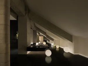Modern bedroom with a black headboard, a bench, white balls, and a cement wall, featuring a minimalist and contemporary aesthetic