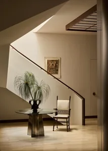 Cozy modern living space with a wooden staircase, glass table, and potted plant, set against white walls and a wooden floor