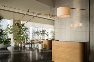 A modern dining space with a wooden floor, a dining table, chairs, and a counter with a sink, surrounded by potted plants and natural light from a large window
