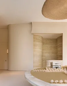 A modern living dining space with a white wall, tan floor, and a dining table surrounded by vases and chairs, featuring a fireplace for warmth and coziness
