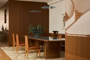 Dining room with a wooden table and chairs, surrounded by a modern living space with a couch in the background, featuring a warm color palette and natural materials