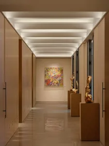 A hallway with a wooden floor and white ceiling, featuring three golden statues on pedestals, creating an elegant and sophisticated atmosphere