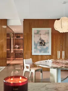 Warm and inviting living space with a wooden floor, glass table, and comfortable seating, featuring a painting on the wall and a vase on the table