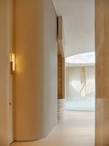 A modern hallway with white marble floors and walls, adorned with artwork, in a dimly lit space with a warm atmosphere