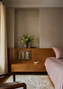 A well-lit bedroom with a bed on the right, a bench on the left, and a vase with flowers on the bench
