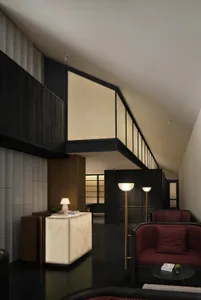 A large, modern room with a high ceiling, featuring a couch, chair, dining table, books, and a potted plant, illuminated by natural light