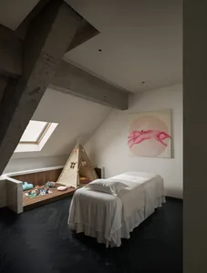 Cozy bedroom with a bed, chair, and painting, decorated with a white color scheme and small items, under a window with natural light