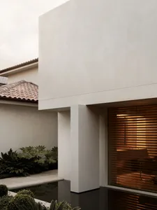 A modern house with a tan exterior, large window, and patio area, surrounded by a residential setting with natural sunlight and a warm atmosphere