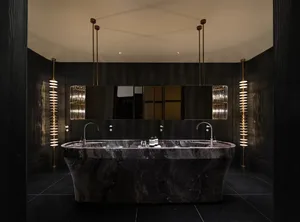 A dimly lit modern bathroom with a large marble bathtub, sink, and mirror