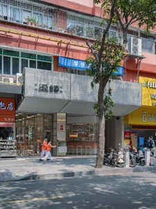 溫暖大地色調的街景，融合現代與傳統建築，兩旁綠樹成蔭，停滿機車，灑落自然陽光