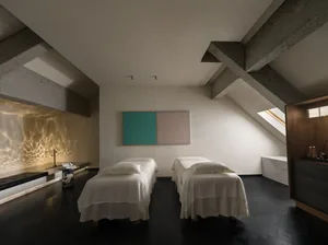 A modern bedroom with a vaulted ceiling, a large white wall with a painting, and a comfortable atmosphere with two beds and a chair