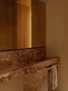 Bathroom with a marble sink, gold faucet, and gold-toned mirror in an elegant and luxurious setting with soft warm lighting
