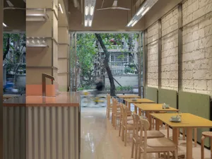A dimly lit restaurant with a modern design, featuring a dining area with a long table and chairs, a kitchen with a counter and appliances, and a person riding a bicycle through the space
