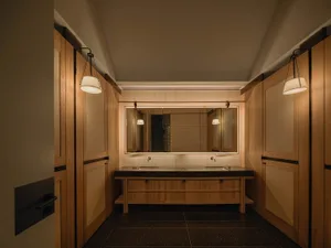 A well-lit bathroom with two sinks under a mirror, a wooden cabinet, and a predominantly white space