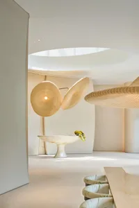 Modern minimalist room with a white floor, a metal bowl on a pedestal, a glass vase, and a light fixture providing illumination