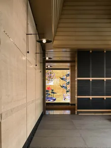 A stone-walled hallway with a mosaic wall featuring a painting of flowers, decorated with chandeliers and wall sconces