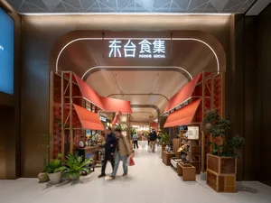 繁忙的現代購物中心，擁有大型拱門與多家商店，人們提著手提包行走其間，周圍擺滿盆栽植物