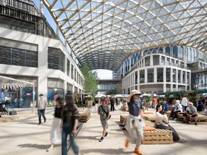 A large, open public space with a glass ceiling, numerous pillars, and a lively atmosphere, filled with people walking, sitting, and engaging in activities