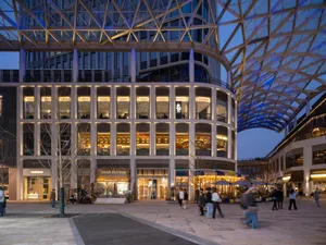 A modern building with a glass and metal facade, featuring a large atrium and glass-covered walkway, with natural light streaming in through the glass windows