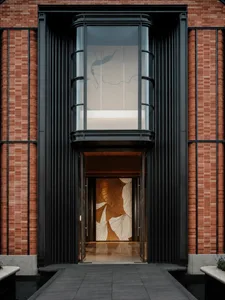A modern building with a brick facade and a large window featuring a gold design, set against a bright and sunny day