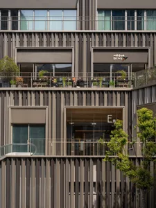 Photograph of a modern building with a metal balcony, concrete walls, and natural light from the side