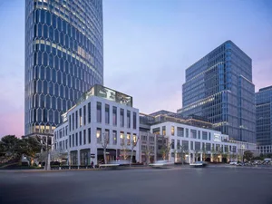 A city street at night with a large glass building, illuminated by streetlights and surrounded by urban life