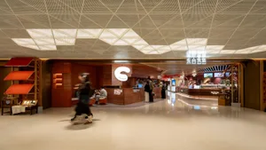 A large, open public space with a shiny floor, modern furniture, and natural light, filled with people walking, sitting, or standing
