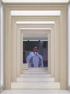A modern hallway with a white color scheme and a man on a screen in the background