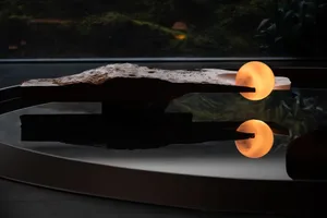 A rock sculpture shaped like a boat sits on a glass table, reflecting light and creating a visually appealing scene