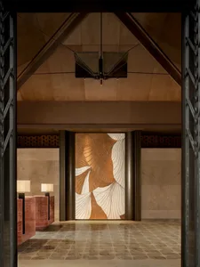 A well-lit lobby with a brown and gold color scheme, featuring a large wooden door, a hanging lamp, and a golden design on the doorway