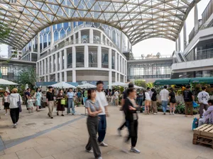 A bustling city street with people walking in various directions, surrounded by a mix of modern and traditional buildings with umbrellas on the sidewalk