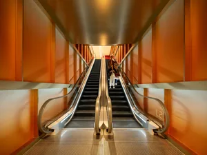 Photograph of an orange-colored building with a metal staircase and people on the second floor, taken in bright daytime lighting