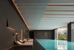 A relaxing outdoor pool area with a patio, chairs, a couch, and potted plants, surrounded by concrete, glass, and metal, bathed in warm natural light