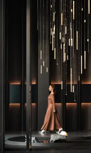 A woman in a pink dress walks in a modern room with a black and white color scheme, a large hanging light fixture, and dim lighting creating a cozy atmosphere
