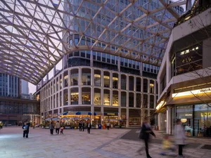 A bustling city street at night with a large building featuring a glass ceiling, surrounded by people and artificial lighting