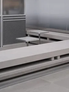 Dining area with a concrete bench and metal table in a well-lit room with a glass wall and cement floor
