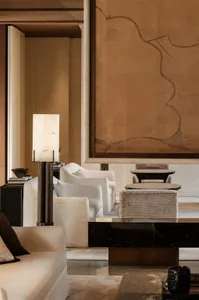 A well-lit living room with a couch, chair, and dining table, featuring a brown wall hanging and a warm atmosphere