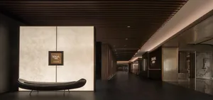 A modern lobby with a wooden floor, white walls, and a couch, featuring a bench in the center of the room