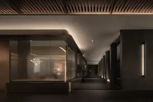 A dimly lit, modern hallway with a glass wall, wooden floor, and a bench in the middle, creating a moody atmosphere